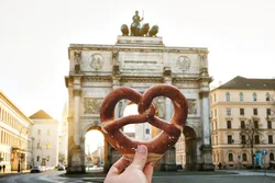 Bretzel allemand à la main sur fond de l'arc de triomphe de la Porte de la Victoire Siegestor à Munich. Allemagne